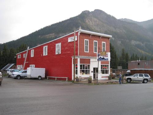 A red two-story building with a sign reading "General Store," surrounded by mountains and parked vehicles.