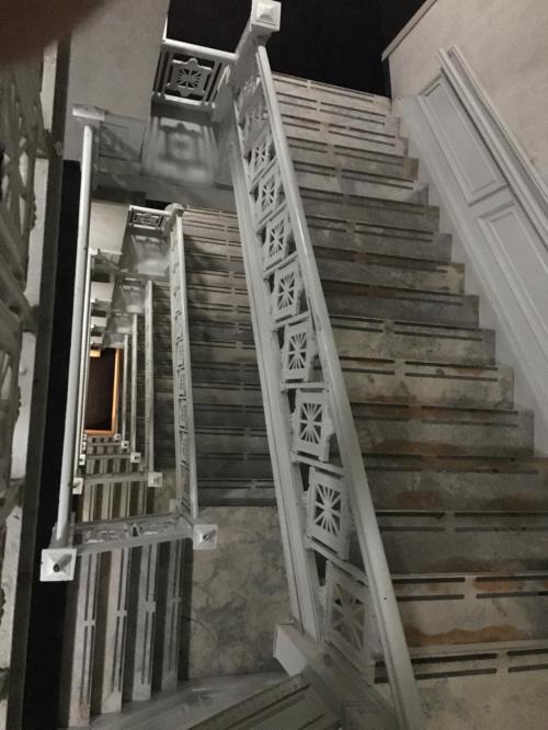 A spiral staircase with ornate white railings and worn steps, viewed from above.
