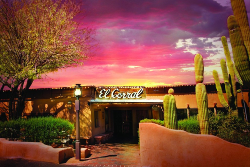 A desert scene at dusk featuring the entrance to El Corral, surrounded by cacti and vibrant pink skies.