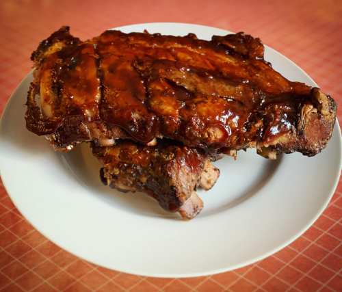 A plate of glazed, barbecued ribs with a rich, sticky sauce, resting on a white dish.