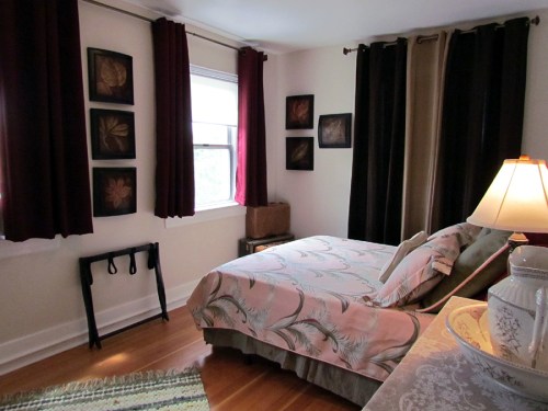 Cozy bedroom with a floral bedspread, dark curtains, and framed artwork on the walls, featuring a lamp and a rug.