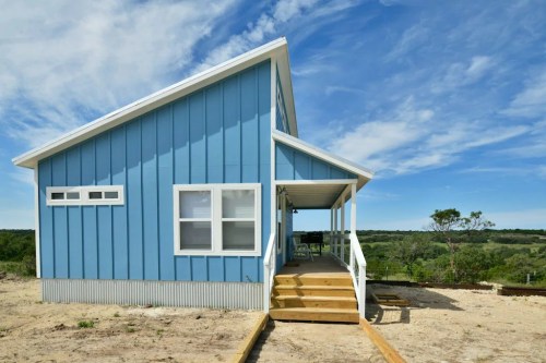 A blue house with a porch, set against a clear sky and green landscape.