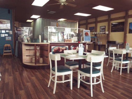 A cozy restaurant interior with wooden floors, tables, and a counter displaying food items. Brightly lit and inviting.