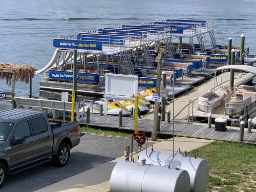 A dock with several pontoon boats and a pickup truck parked nearby, set by a calm waterway.