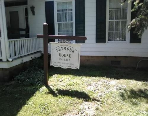 Sign for Seymour House, established in 1836, in front of a white house with green shutters and a porch.