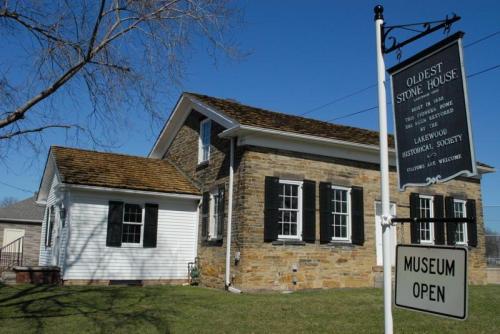 Historic stone house with a sign reading "Oldest Stone House" and "Museum Open," surrounded by grass and trees.
