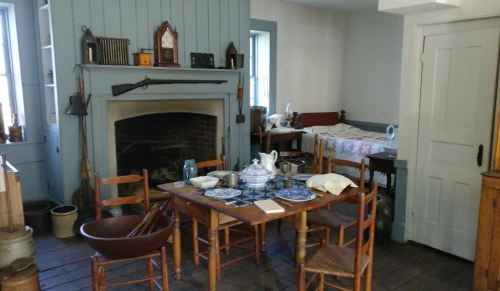 A cozy, vintage kitchen with a wooden table, chairs, a fireplace, and various kitchenware on display.
