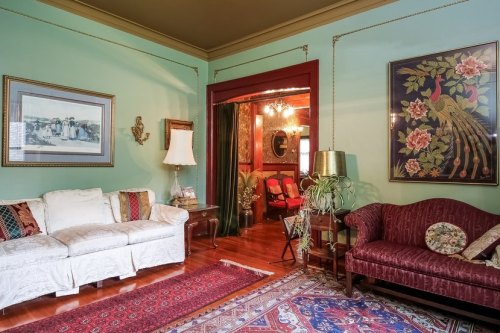 Cozy living room with green walls, vintage furniture, a lamp, and a doorway leading to a red-themed room.