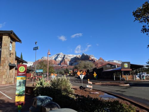 Scenic view of a snowy mountain backdrop with a street and buildings in a small town under a clear blue sky.