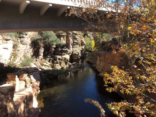 A serene river flows beneath a bridge, surrounded by rocky cliffs and autumn foliage.
