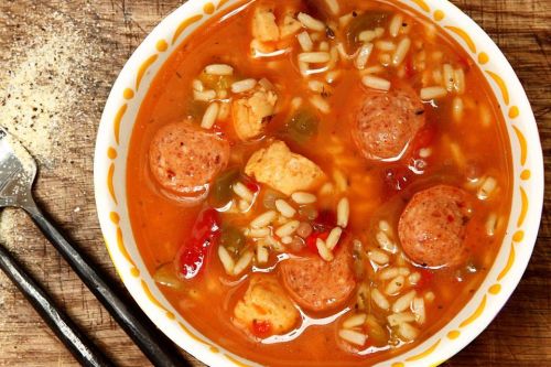 A bowl of hearty soup with meatballs, rice, and vegetables in a rich broth, garnished with herbs.