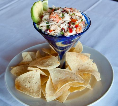 A colorful seafood ceviche served in a martini glass, garnished with lime, alongside a plate of tortilla chips.