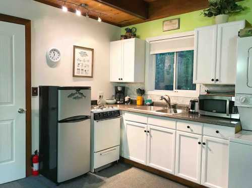 A cozy kitchen with white cabinets, a silver fridge, stove, and a window overlooking greenery.