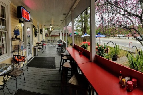 A cozy outdoor dining area with tables, a red bar, and blooming trees, inviting guests to enjoy a meal.
