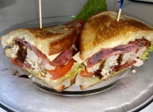 A close-up of a sliced sandwich with layers of meat, cheese, lettuce, and tomato, served on a plate.