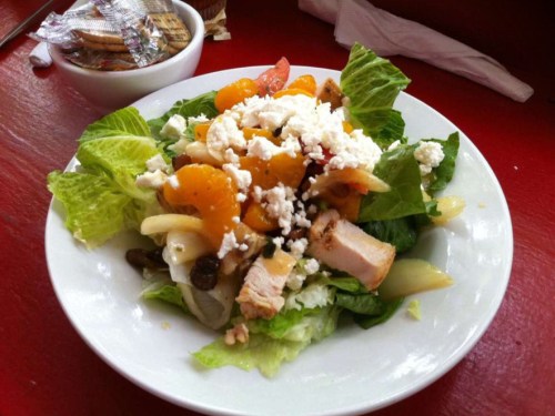 A fresh salad with lettuce, chicken, mandarin oranges, cheese, and various toppings on a white plate.