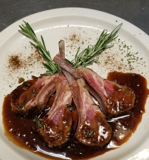 A plate of lamb chops garnished with rosemary and drizzled with a rich sauce, sprinkled with herbs.