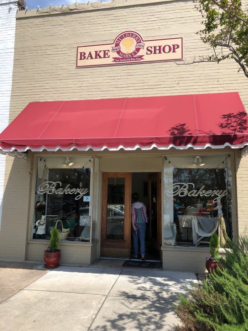 A quaint bake shop with a red awning, featuring large windows and a welcoming entrance.