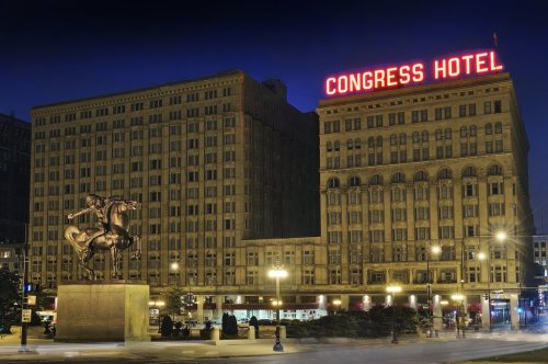 Night view of the Congress Hotel with a statue in front, illuminated by bright neon lights.