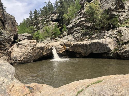 A serene natural scene featuring a small waterfall cascading into a calm pool, surrounded by rocky cliffs and greenery.