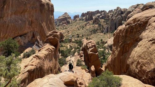 A scenic view of rocky terrain with hikers navigating a trail between towering red rock formations.