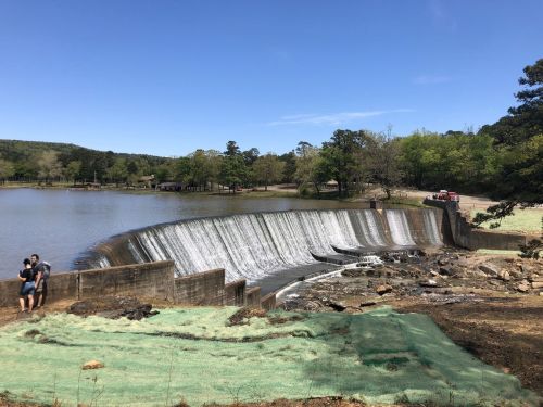 A scenic view of a waterfall cascading over a dam, with two people sitting nearby and lush greenery in the background.