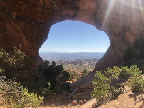 A scenic view through a rock arch, showcasing a landscape of hills and trees under a clear blue sky.