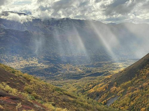 A scenic mountain landscape with rays of sunlight illuminating a valley filled with autumn foliage.