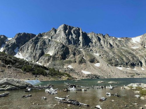 A serene mountain landscape with rocky peaks, a clear blue sky, and a calm lake reflecting the surroundings.