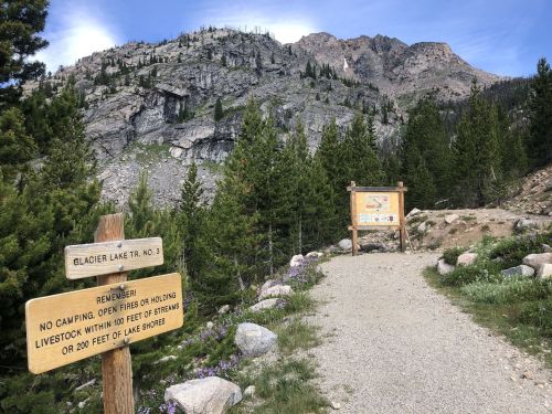 Trailhead for Glacier Lake Trail No. 3, with signs about regulations and a scenic mountain backdrop.