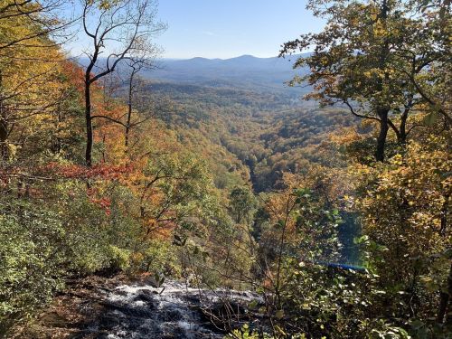 A scenic view of a valley filled with autumn foliage, with mountains in the distance under a clear blue sky.