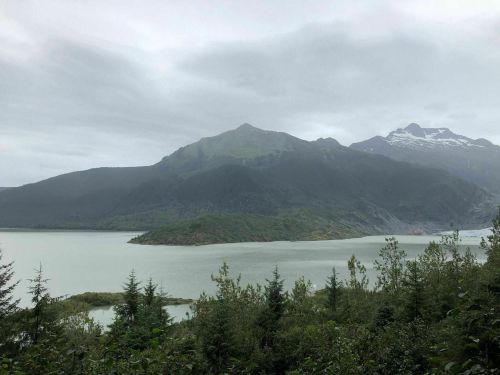 A serene landscape featuring a lake surrounded by mountains and lush greenery under a cloudy sky.