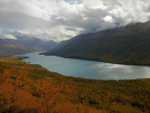 A serene lake surrounded by mountains and autumn foliage under a cloudy sky.