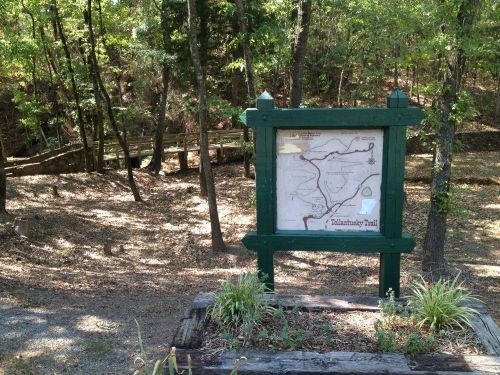 A wooden sign displaying a map of the Tallahatchie Trail, surrounded by trees and a natural landscape.