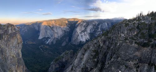 A panoramic view of Yosemite Valley, showcasing towering cliffs and lush greenery under a clear sky at sunset.