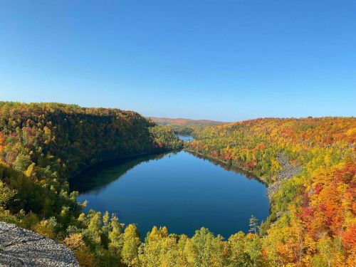 A serene lake surrounded by vibrant autumn foliage under a clear blue sky.