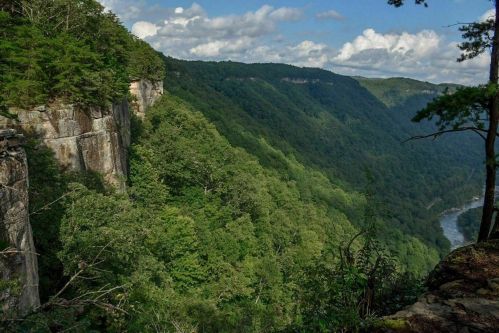 Lush green mountains and cliffs under a partly cloudy sky, with a river winding through the valley below.