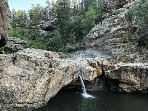 A serene landscape featuring a small waterfall cascading into a tranquil pool, surrounded by rocky terrain and trees.