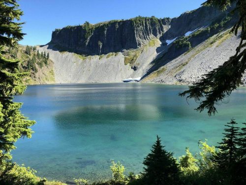 A serene lake surrounded by rocky cliffs and lush greenery under a clear blue sky.