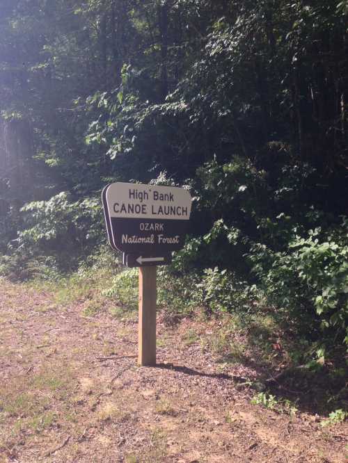 Sign for "High Bank Canoe Launch" in Ozark National Forest, surrounded by trees and a dirt path.