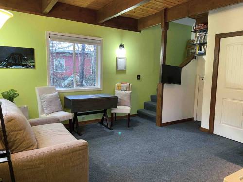 Cozy living space with green walls, a sofa, a small table, and stairs leading to an upper level. Natural light from a window.