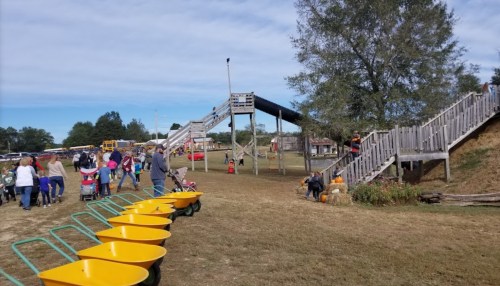 A playground with slides and ramps, surrounded by families and wheelbarrows, on a sunny day.