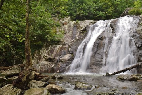 A serene waterfall cascading over rocky terrain, surrounded by lush green trees and a calm river below.