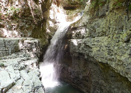 A serene waterfall cascading down rocky cliffs into a tranquil pool below, surrounded by lush greenery.