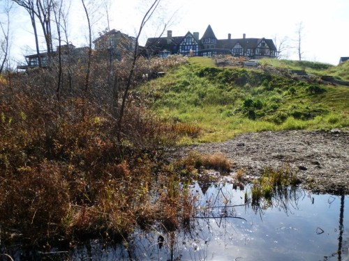 A scenic view of a grassy hill with a large building in the background, reflecting in a small pond in the foreground.