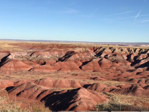 Vast landscape of red and brown hills under a clear blue sky, showcasing the unique geological formations of the area.