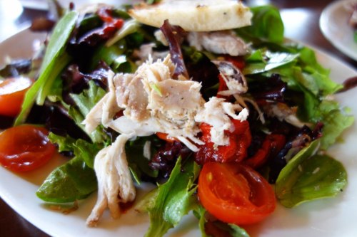 A fresh salad with mixed greens, cherry tomatoes, shredded chicken, and roasted red peppers on a white plate.