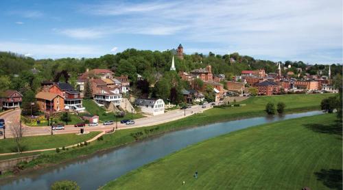 A scenic view of a small town along a river, surrounded by green hills and dotted with historic buildings.