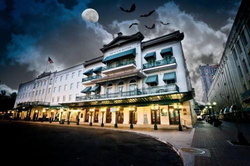 A historic hotel at night, with a full moon and bats flying in a cloudy sky.
