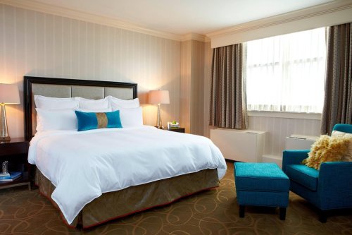A cozy hotel room featuring a large bed, blue accent chair, and soft lighting from bedside lamps.